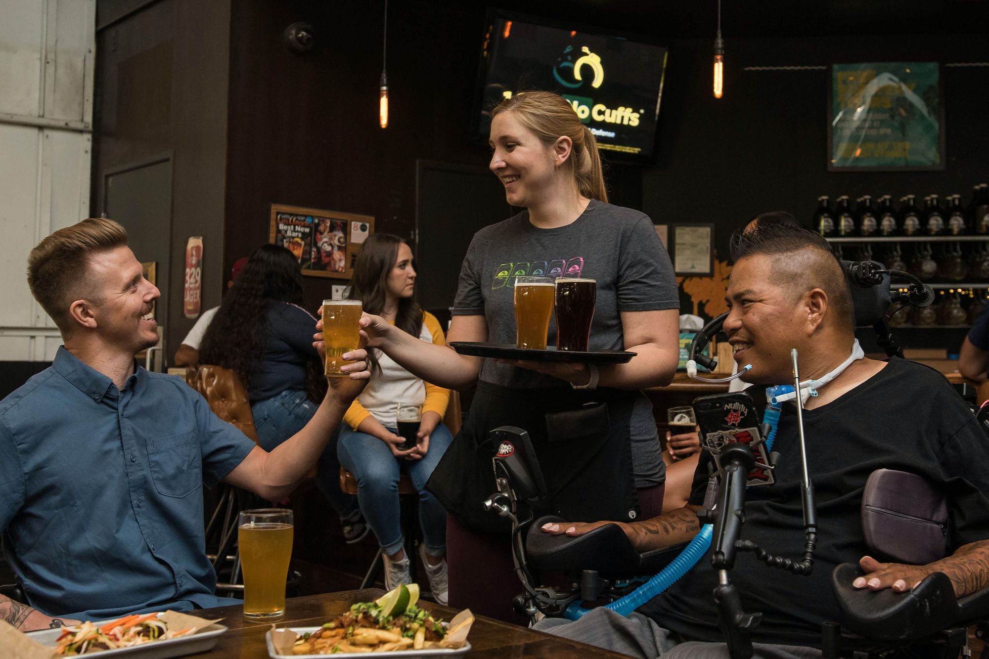 photo of a female waitress serving a beer to customers, one of which is physically disabled